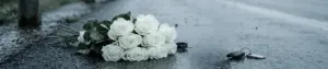 White bouquet of roses lies on a wet street near a car key fob and keyring after rain, suggesting loss or mourning in an urban setting.